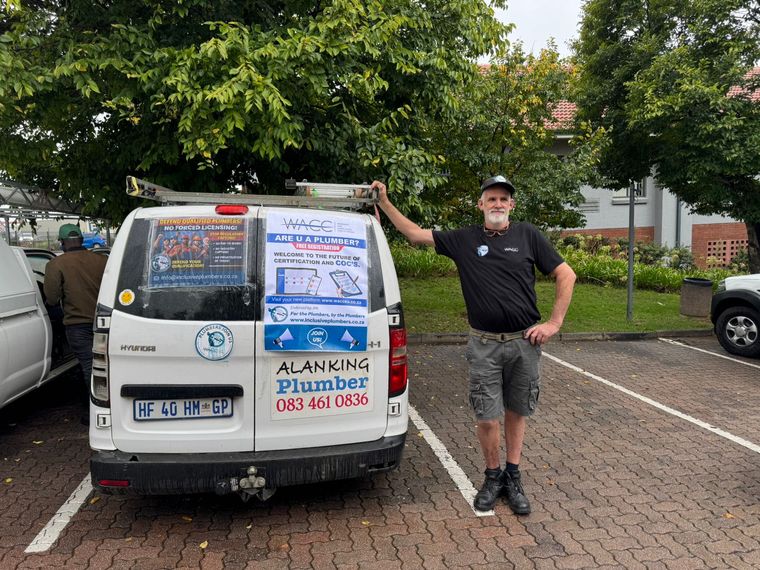 A plumber standing beside his van, its rear windows carrying IPA and WACC campaign posters