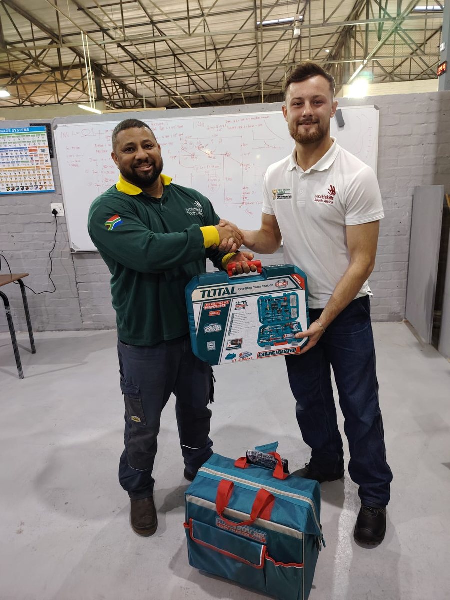 An IPA representative handing a tool set to a student in a training workshop, both in WorldSkills South Africa shirts